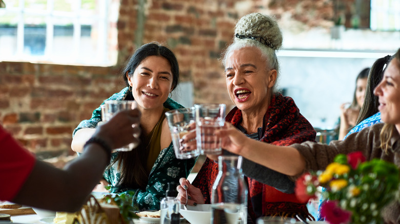 Small group of people holding water glasses at lunch table, celebration, smiling, happiness, bonding