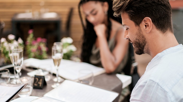A young diverse couple on a romantic date, sitting at a table on an outdoor restaurant terrace and reading the menu