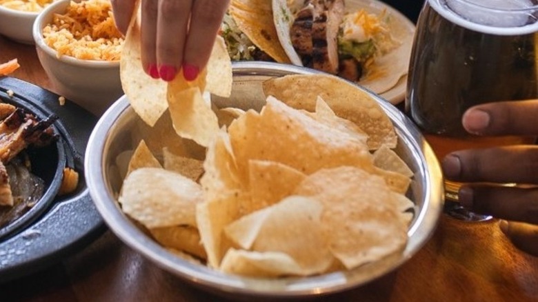 Hand grabbing tortilla chip out of metal bowl