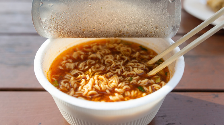 a white plastic cup full of hot instant ramen with chopsticks in it