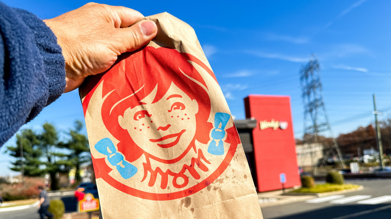 Holding a Wendy's bag in front of Wendy's restaurant