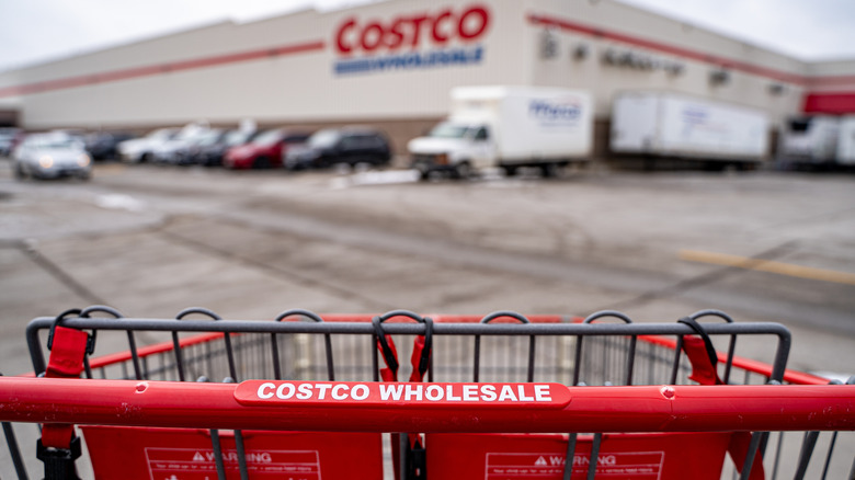 A Costco shopping cart in the parking lot, with the store signage in the distance