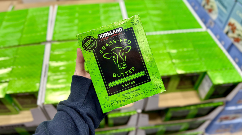 Holding a green bulk box of Kirkland Signature Grass-Fed Butter in front of the store display