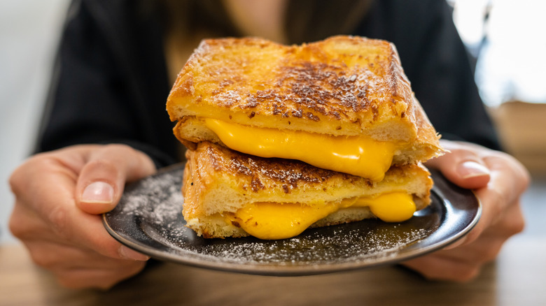 A woman holds up a grilled cheese sandwich on a plate