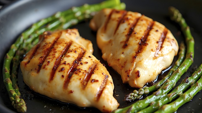 Two grilled chicken breasts on a plate with asparagus spears