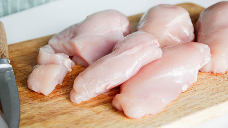 Raw chicken breast on a cutting board next to a knife