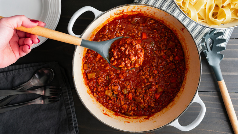 Hand holding serving spoon of meaty spaghetti sauce