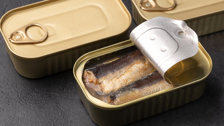 Opened tin of sardines with unopened tins on dark background