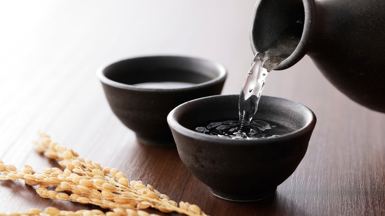 Japanese sake being poured into two small black cups to drink from