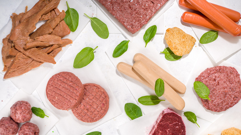 A spread of plant-based meats on a white background with spinach leaves scattered about