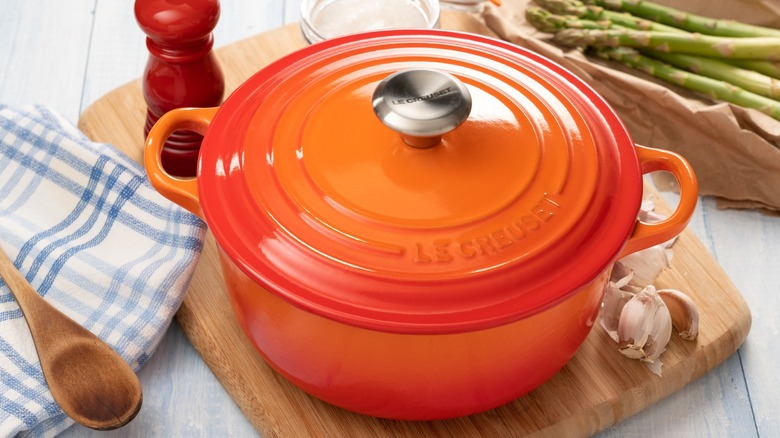 Le Creuset Dutch oven on wood board with garlic and pepper grinder