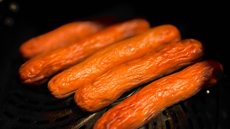 Five hot dogs cooking in an air fryer basket.