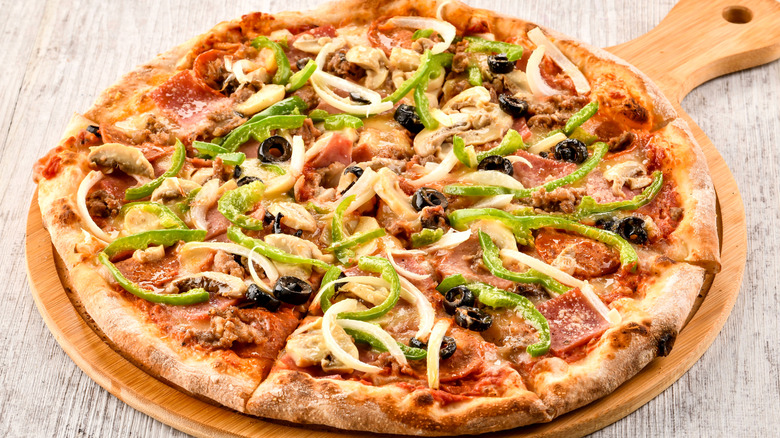 A pizza on a wooden tray topped with green peppers, black olives, and onions