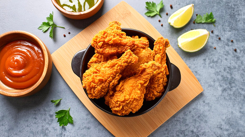 Fried chicken in a bowl on a wooden platter with two sauces and lemon wedges