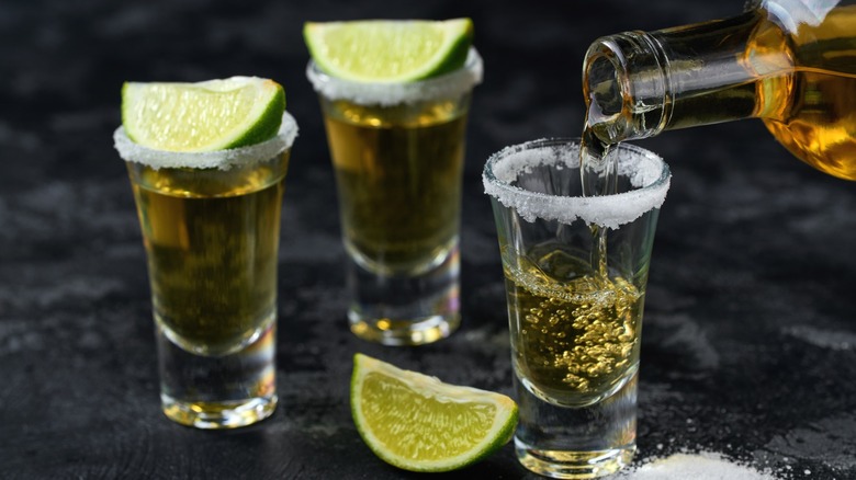 Tequila being poured into three shot glasses with slices of lime and salt rims