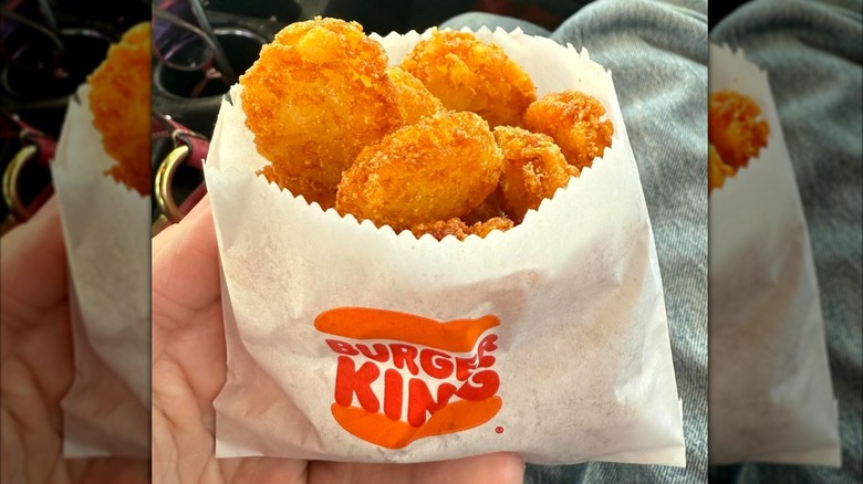 Hand holding small paper packet of Burger King hash browns