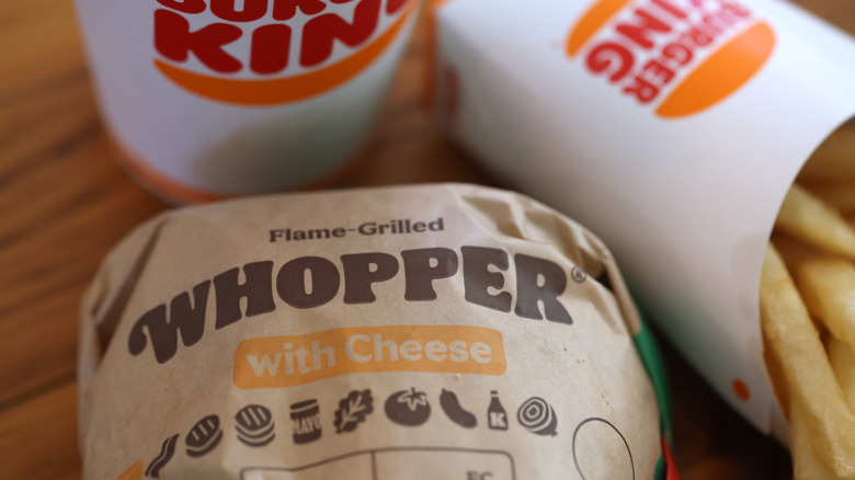 A Whopper with Cheese wrapped in paper beside a Burger King drink cup and french fries