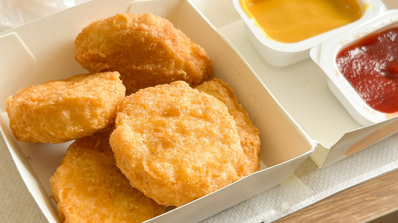 A white box of McDonald's chicken nuggets next to two containers of sauces