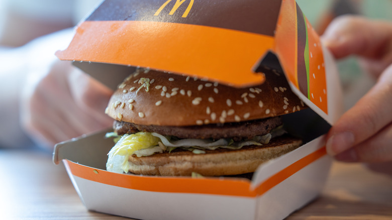 Closeup of a person opening a McDonald's box that contains a Big Mac Cheeseburger
