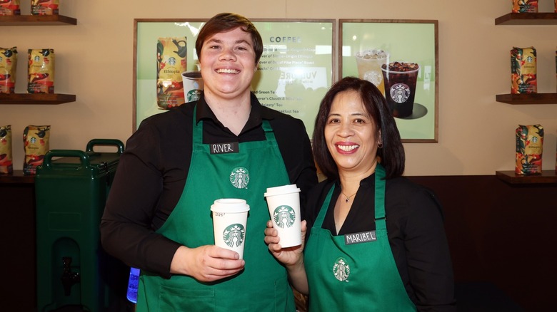 Male and female baristas pose with Starbucks drinks.