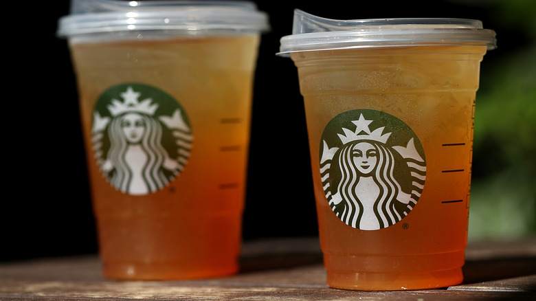 Two cups of Starbucks' iced tea sitting on a wooden surface.
