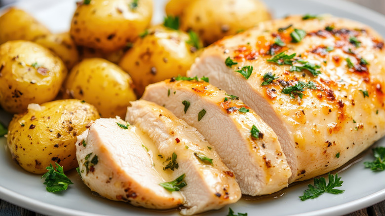 Sliced garlic chicken with small cooked potatoes beside it on a plate