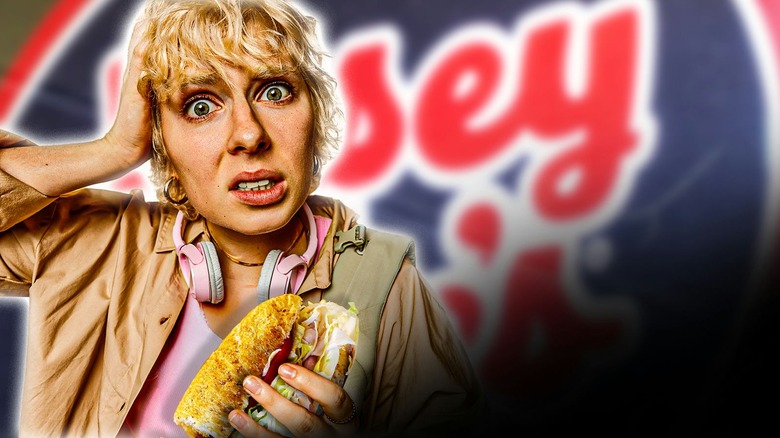 Woman holding a Jersey Mike's sandwich infront of a Jersey Mike's sign
