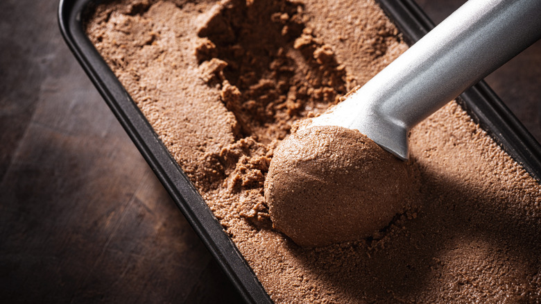 Chocolate ice cream being scooped out of a tub.