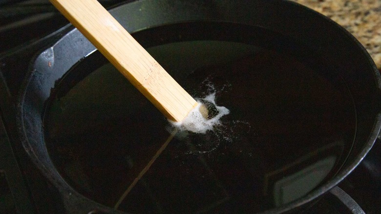oil and a wooden stick in a black frying pan