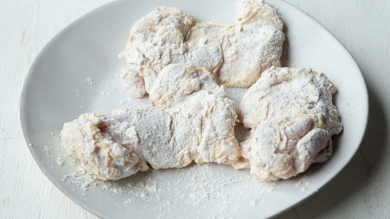 raw chicken covered with flour on a white plate