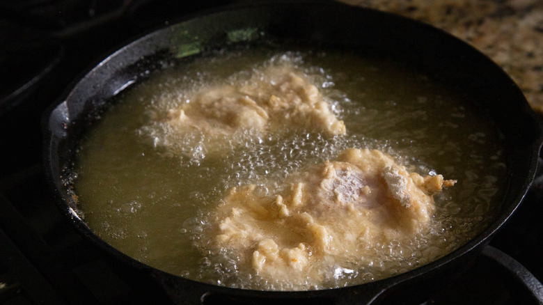 chicken strips frying in a black pan