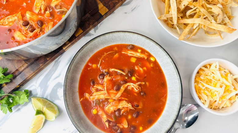 Bowl of chicken tortilla soup surrounded by various toppings