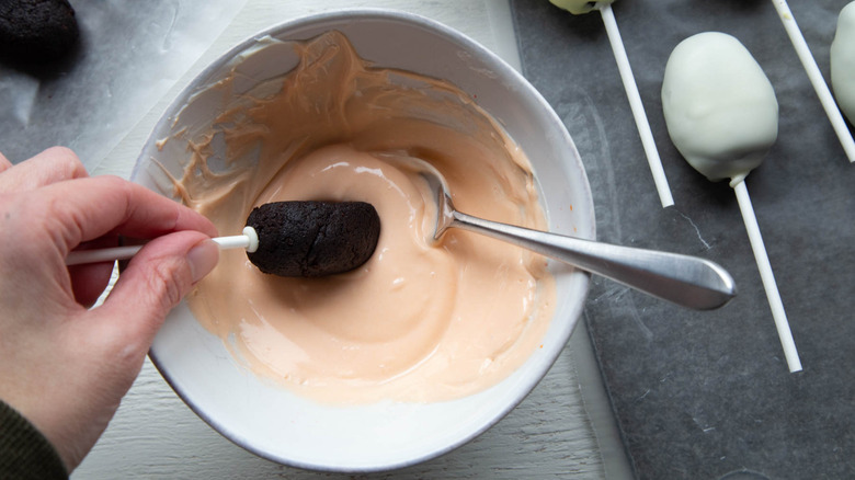 hand dipping cake pop into orange glaze