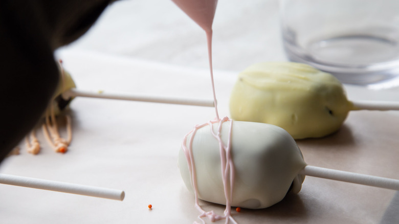hand drizzling pink glaze over white cake pop