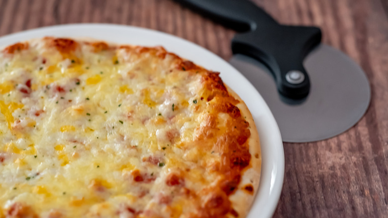 Cheese pizza on plate with pizza cutter on side.