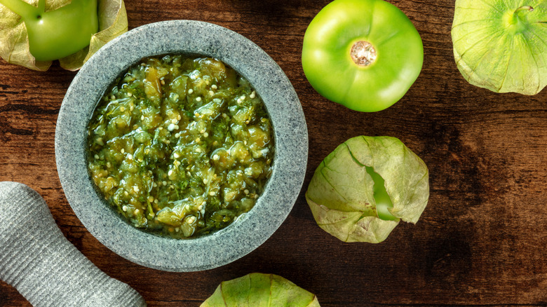 Stone bowl with green salsa verde on a board with tomatillos