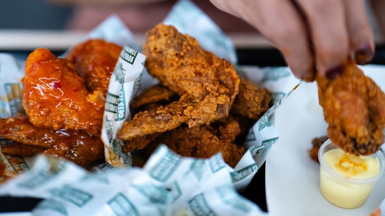 Chicken wings from wingstop next to a hand dipping a wing in a white sauce