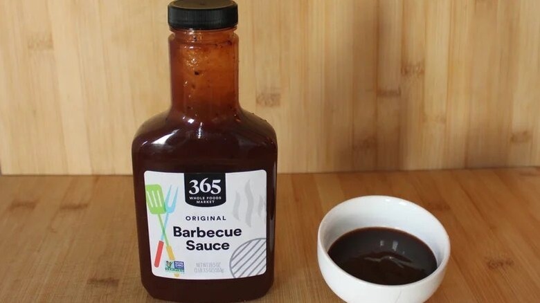 A bottle of 365 barbecue sauce, with a small bowl of the stuff next to it.
