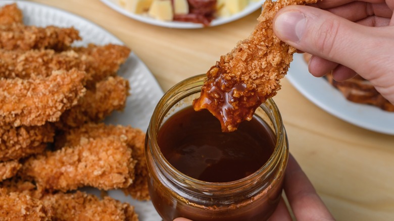 Chicken tenders being dipped in barbecue sauce.