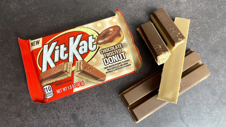 A package of chocolate frosted donut Kit Kat near pieces of the candy on a table.