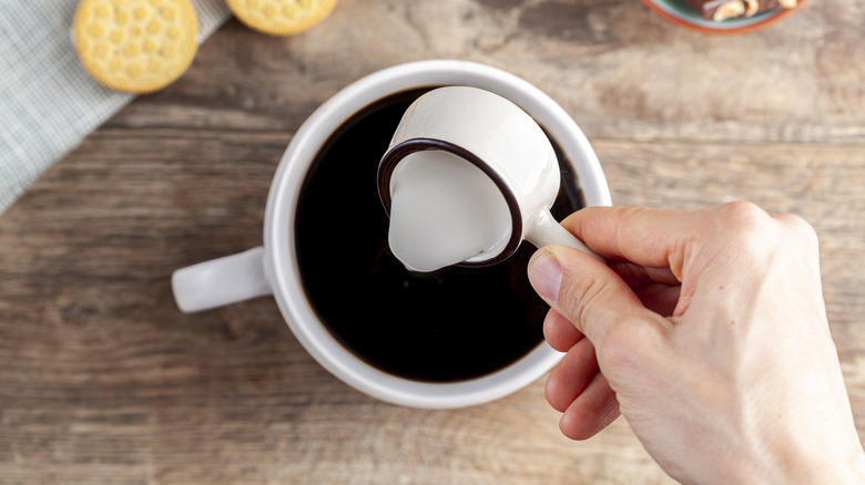 Hand pouring creamer into coffee