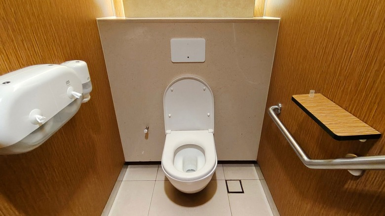 Restroom interior with a white toilet, wood-paneled walls, and a metal grab bar