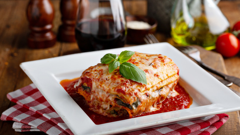 Lasagna with tomato sauce and basil leaf on square plate.