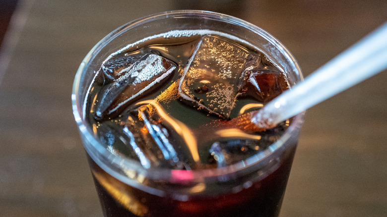 A close-up shot of a bubbly glass of cola with ice and a straw