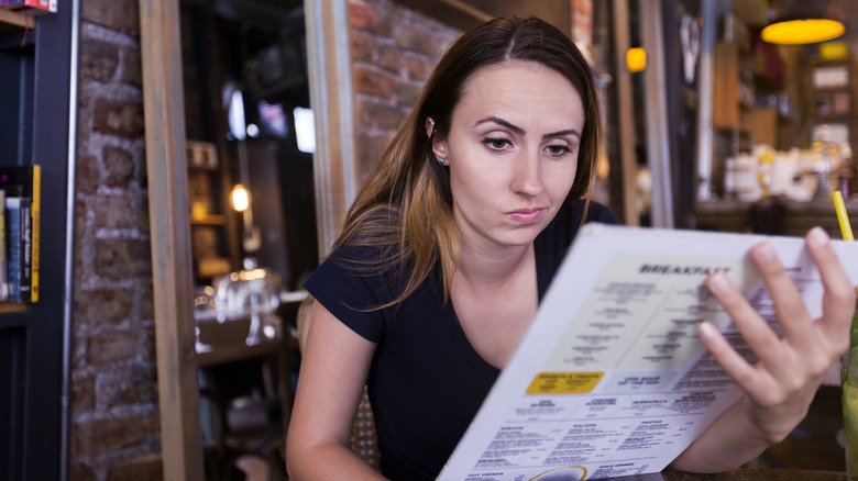 woman looking skeptically at a restaurant menu