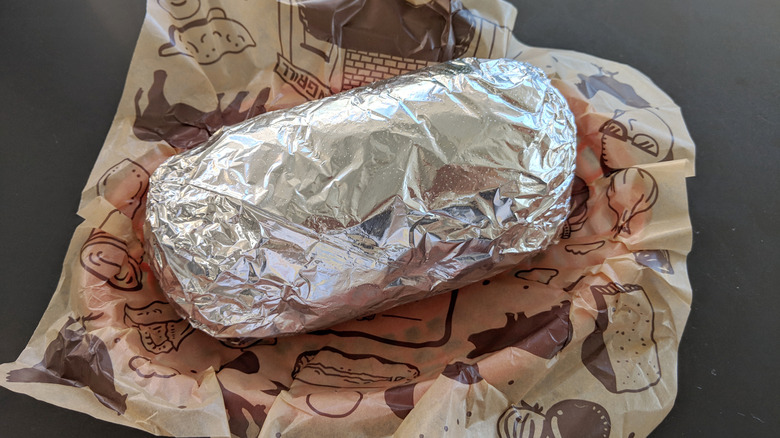 A Chipotle burrito wrapped in foil, on printed parchment paper