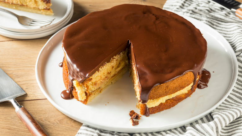 A Boston cream pie missing a slice on a white serving plate