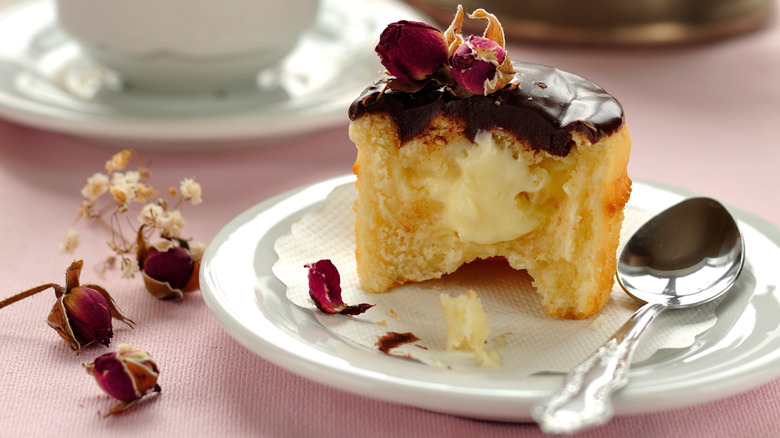 An individual Boston cream pie on a plate with dried rosebuds and a spoon