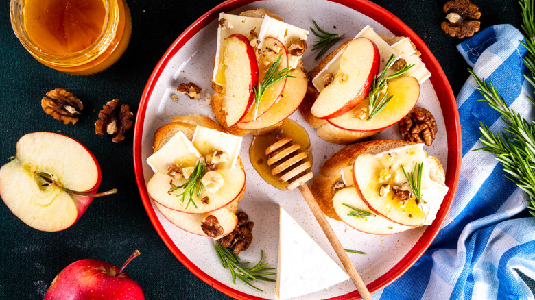 Sliced apples and cheese on top of crostini on a plate garnished with honey and rosemary