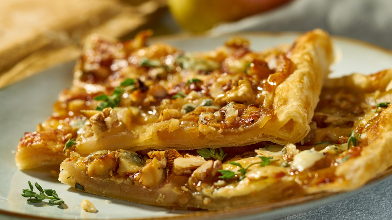 A closeup of a walnut, apple, blue cheese flatbread with flaky crust